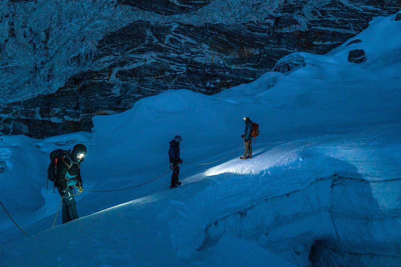 Climbers crossing a crevasse by headlamp before dawn
